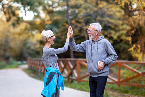 Mature couple taking high five with hands afther jogging in public park